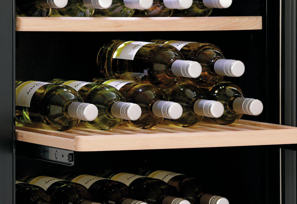 Weinflaschen lagern in einem Weinregal aus Holz. Die Flaschen sind mit Weißwein gefüllt. Das Regal befindet sich in einem dunklen Schrank.