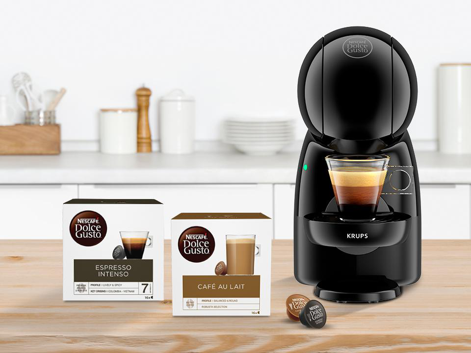 Eine schwarze Dolce Gusto Kaffeemaschine mit Kapseln und einer Tasse Kaffee.