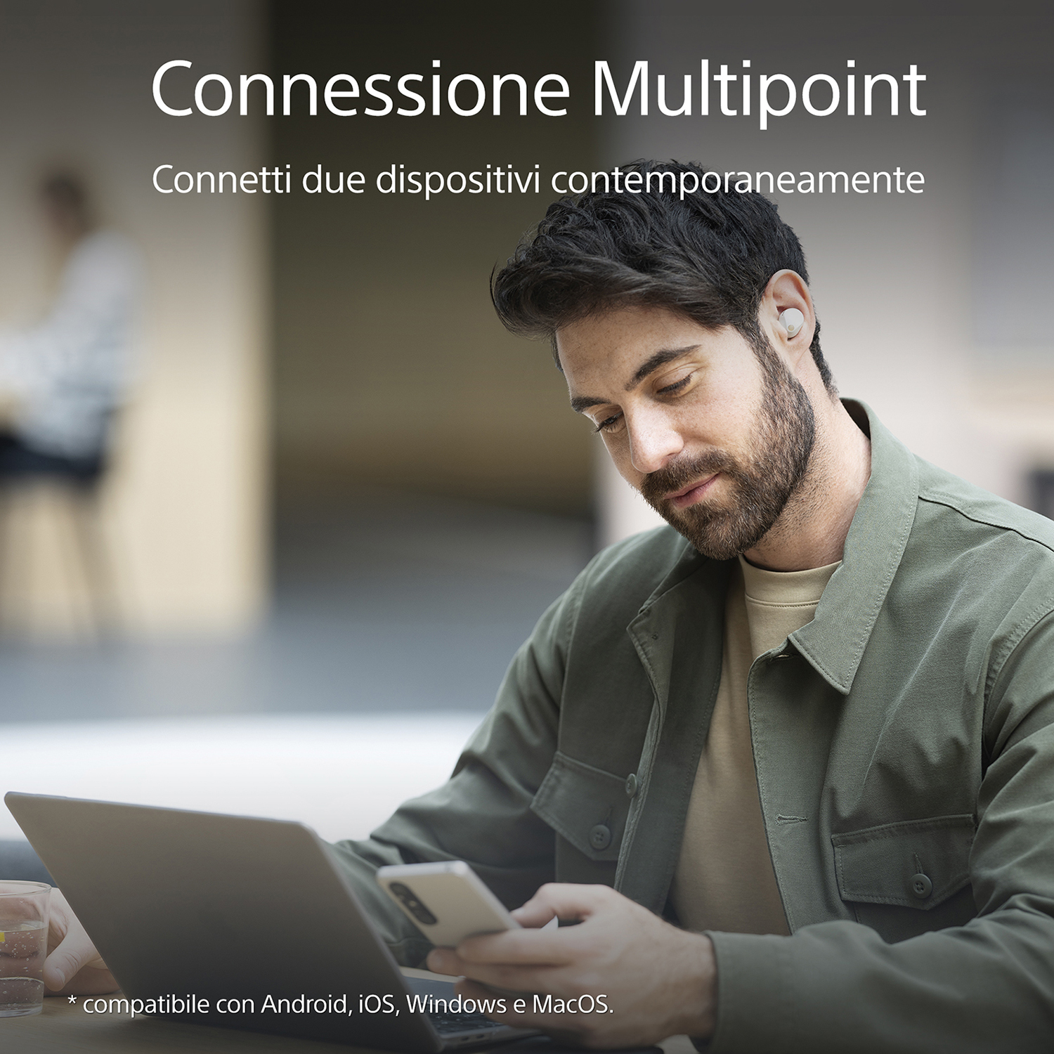 Uomo con auricolari, che utilizza contemporaneamente un laptop e un telefono.