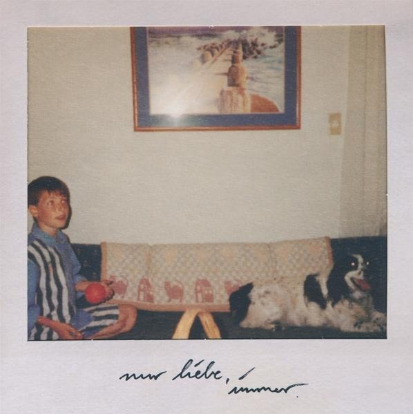 Polaroid-Foto. Junge mit Ball, Hunde auf Couch, Gemälde darüber. Handschriftlicher Text.