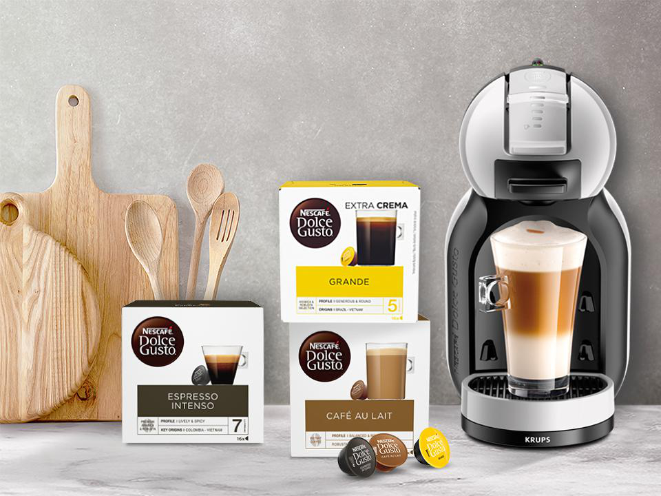 Eine Kaffeemaschine mit Kaffeepads und -boxen. Schneidebretter und Löffel im Hintergrund.