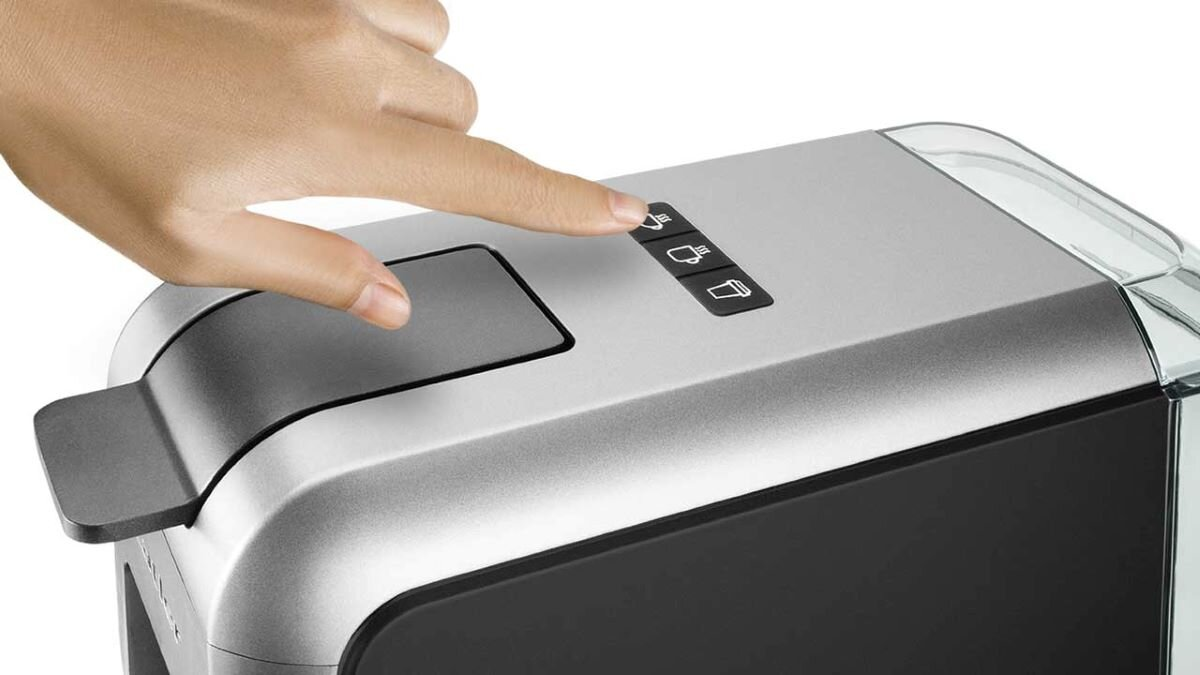 Ręka naciskająca przycisk na srebrno-czarnym ekspresie do kawy.