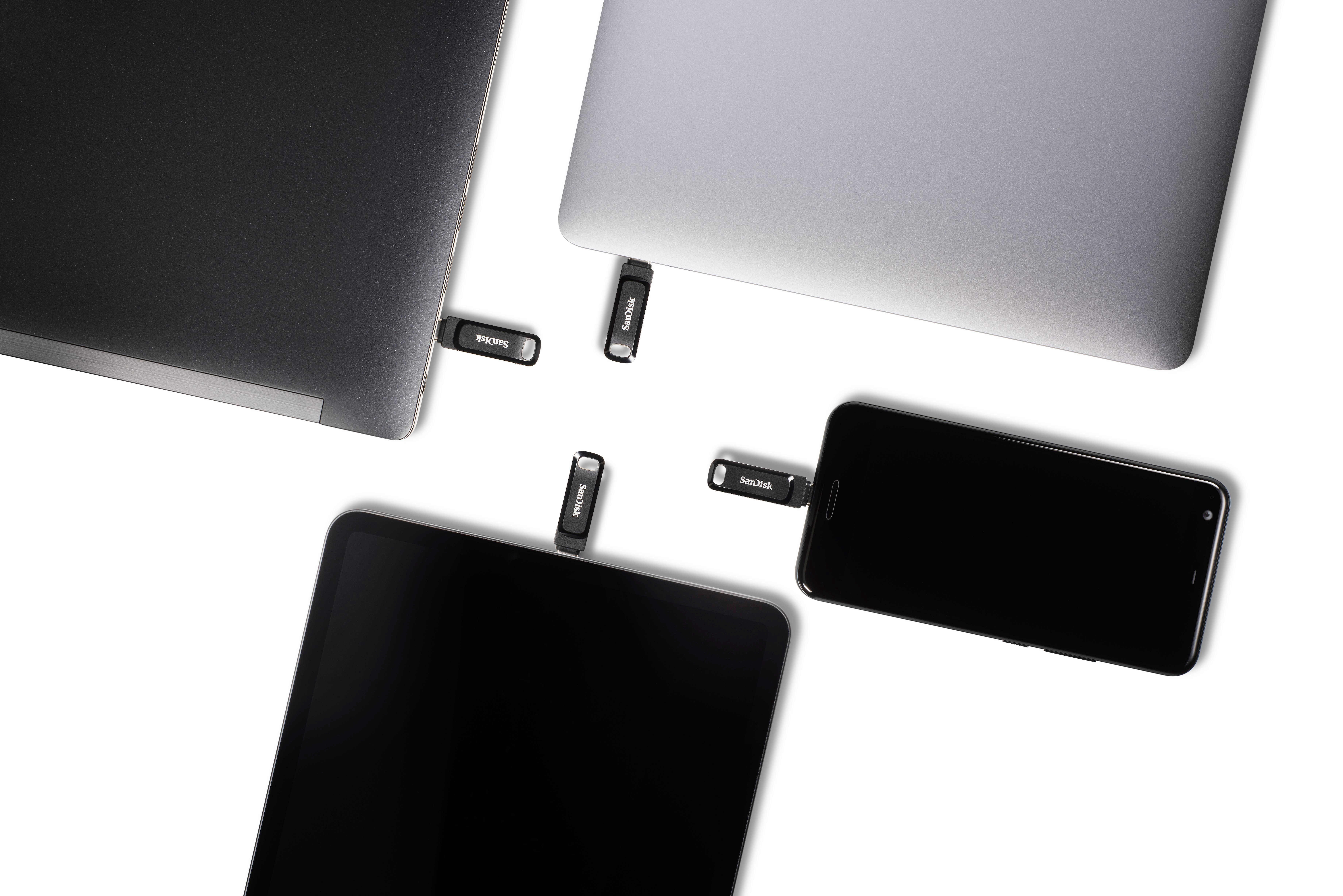 Mehrere USB-Laufwerke, die an Laptops, ein Tablet und ein Telefon angeschlossen sind. Draufsicht.