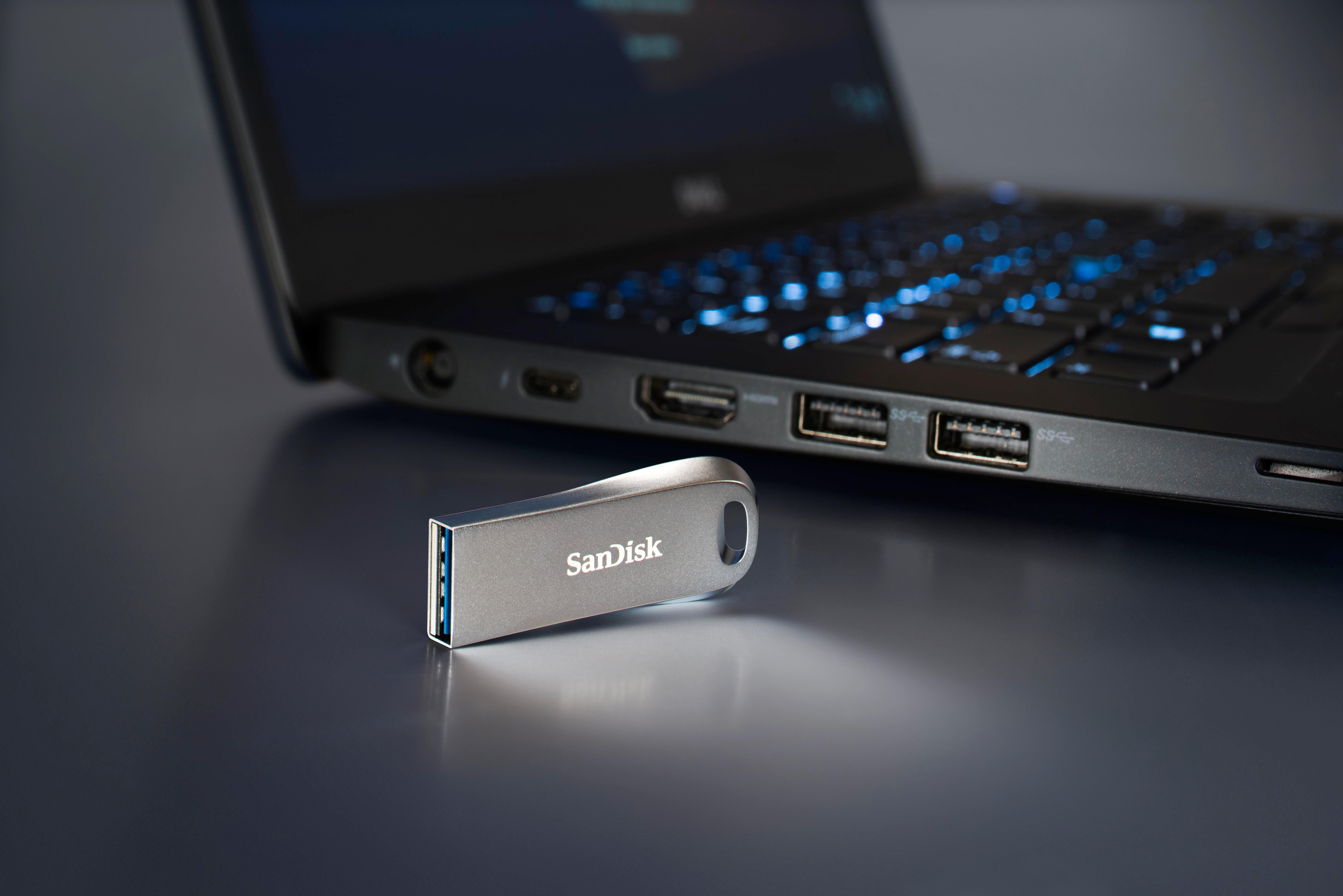 Silberner SanDisk USB-Stick neben einem schwarzen Laptop. Der Laptop ist geöffnet.