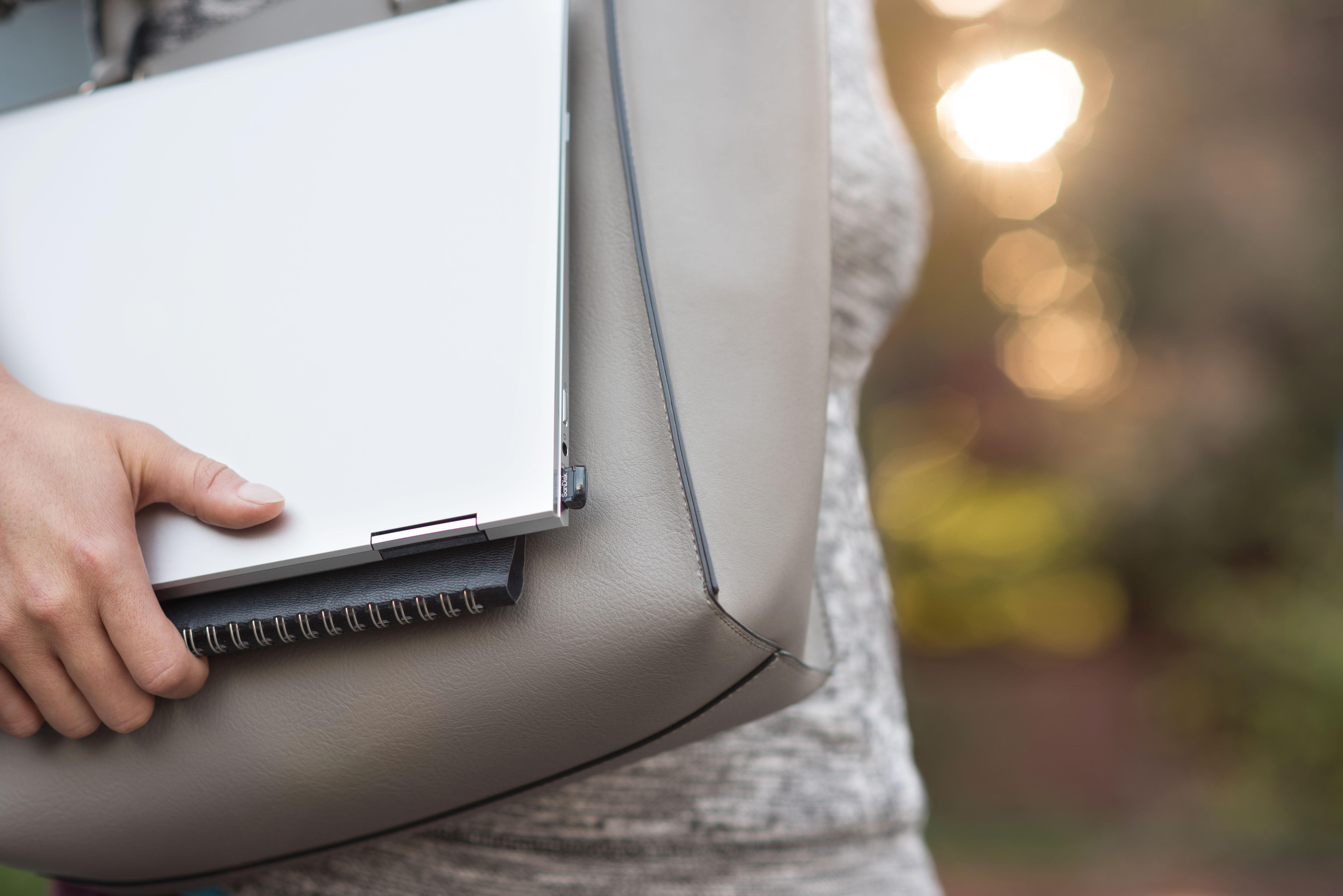 Frau hält Laptop und Notizbuch in einer grauen Tasche.