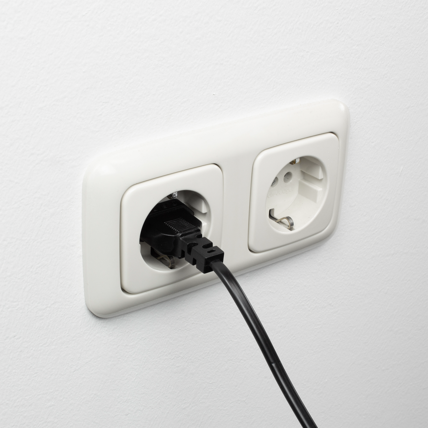 Wit dubbel stopcontact op een witte muur met een zwarte kabel.