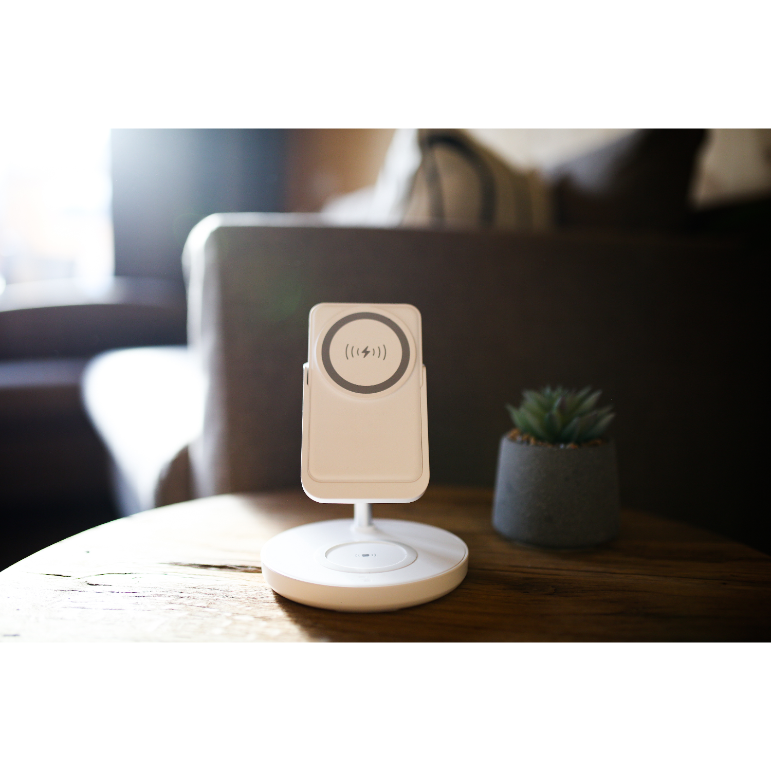 A white wireless charger with a phone on top and a small plant beside it.
