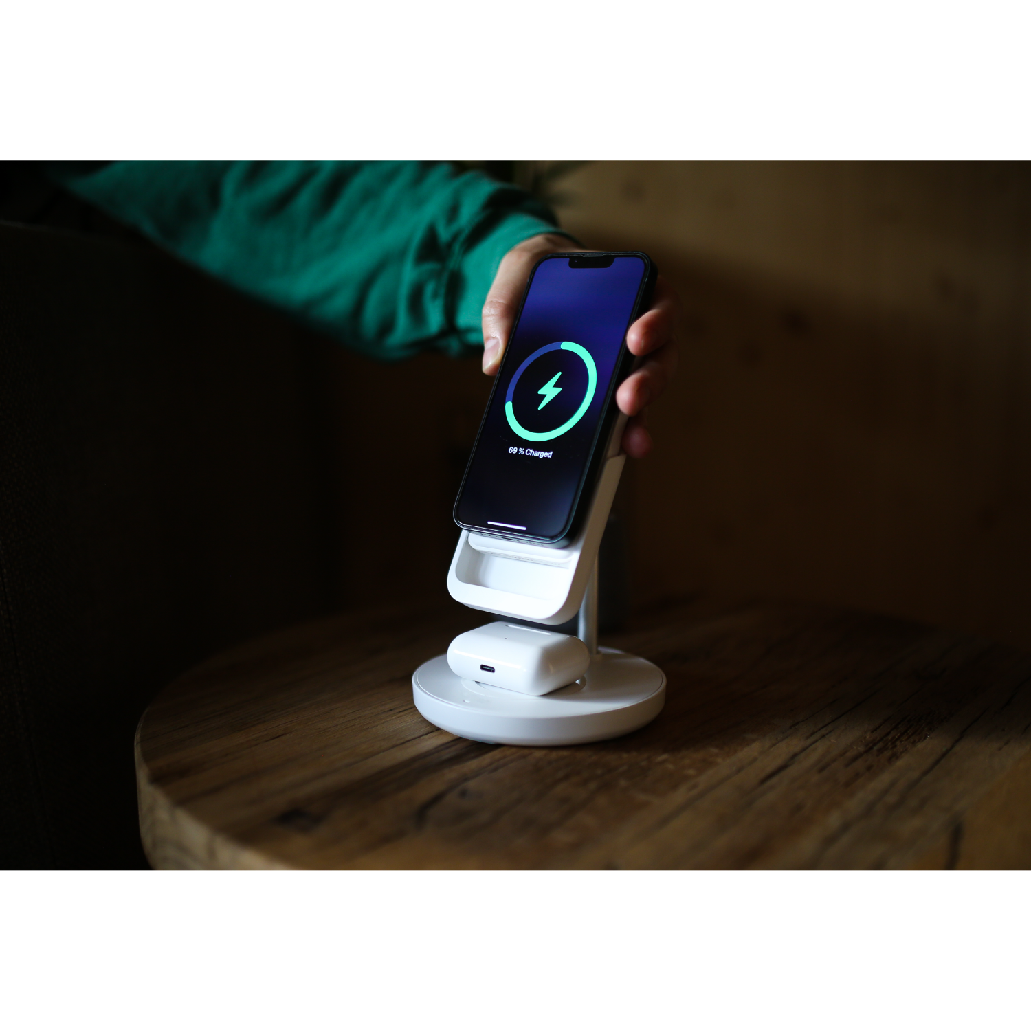 A phone charging on a white stand, with the display showing a charging indicator, on a wooden table.