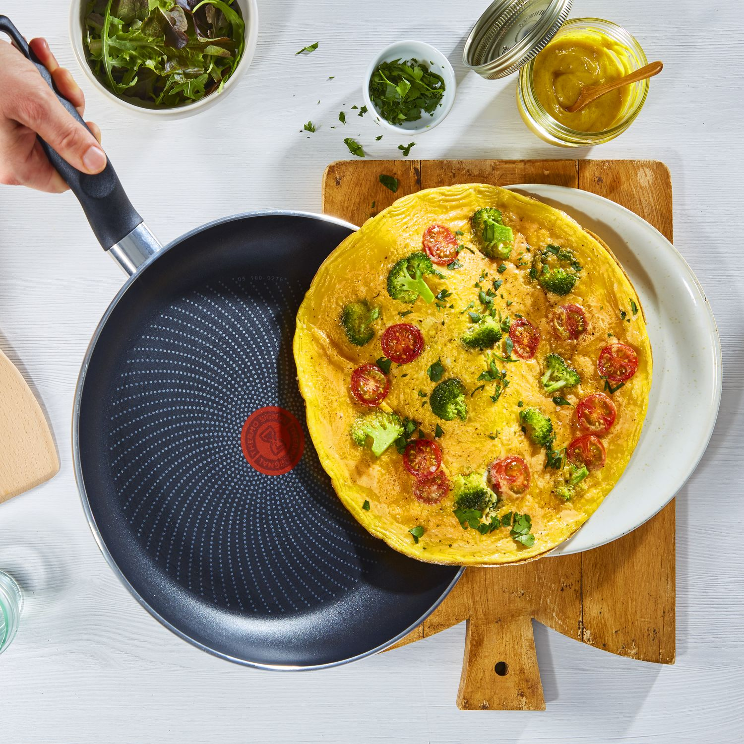 Omelet op houten plank met ingrediënten. Hand houdt pan met omelet vast. Bovenaanzicht.