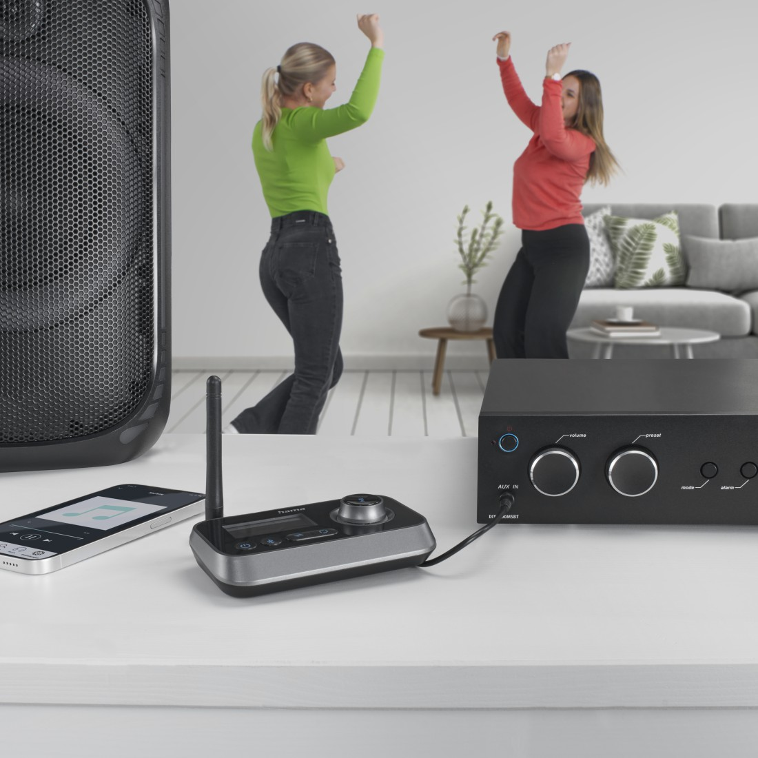 Zwei Frauen tanzen in der Nähe eines Lautsprechers, eines Smartphones und eines Receivers.