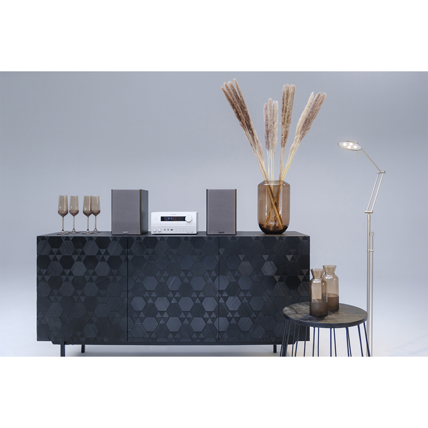 Mobile nero con decorazioni, stereo, altoparlanti, vasi e lampada da terra su sfondo grigio.
