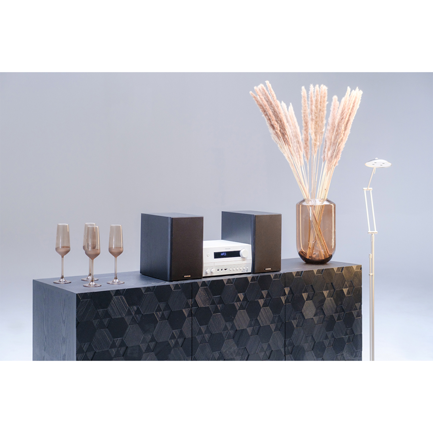 Un mobile scuro con altoparlanti, calici di champagne e un vaso con piante essiccate.