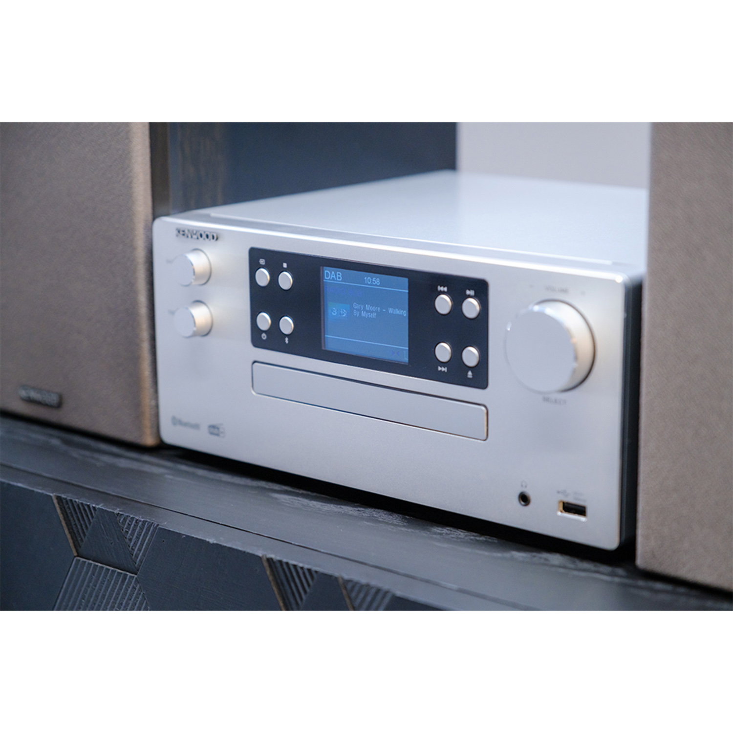 Impianto stereo Kenwood argento su una mensola nera. Lo stereo ha un display e pulsanti.