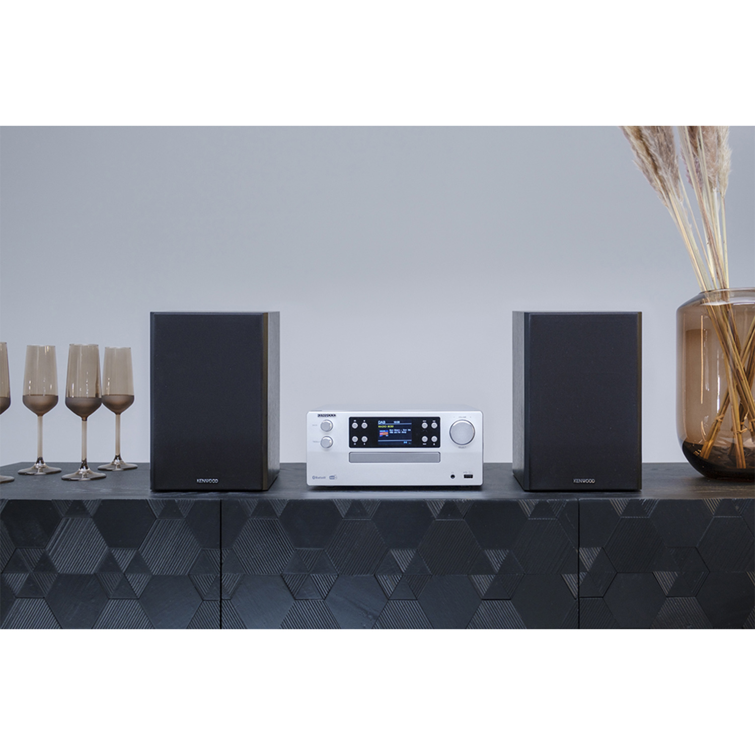 Componenti dell'impianto stereo. Due altoparlanti neri, ricevitore argentato. Bicchieri su superficie scura.