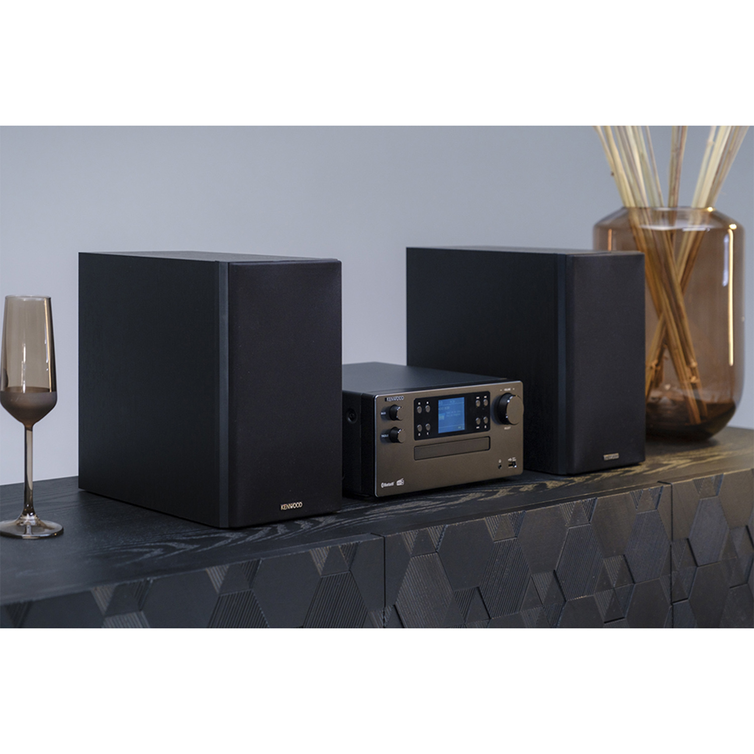 Impianto stereo su superficie in legno scuro. Due altoparlanti, un ricevitore e un vaso.