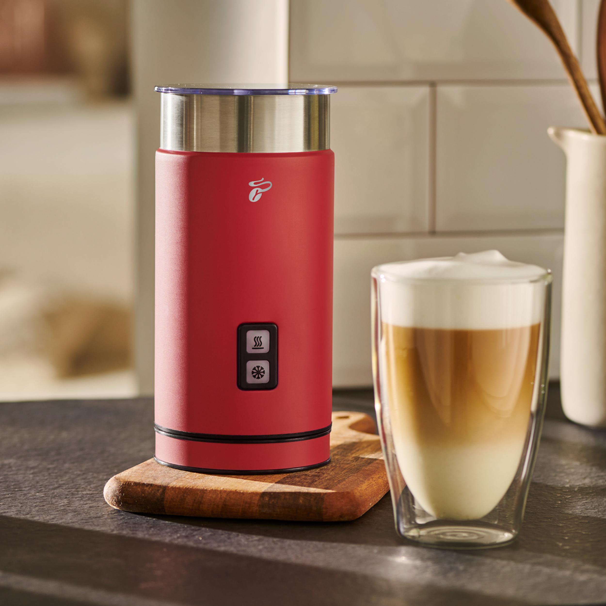 Roter Milchaufschäumer mit einem Glas geschichtetem Latte und einem Holzbrett.