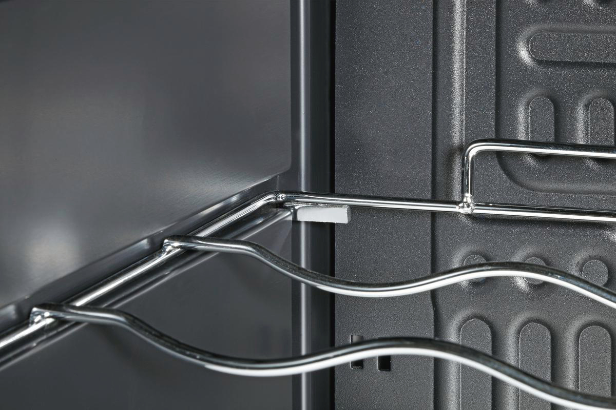 Nahaufnahme eines dunklen Kühlschrankinnenraums mit Metallregalen und grauen Wänden. Die Metallregale haben ein wellenförmiges Design.
