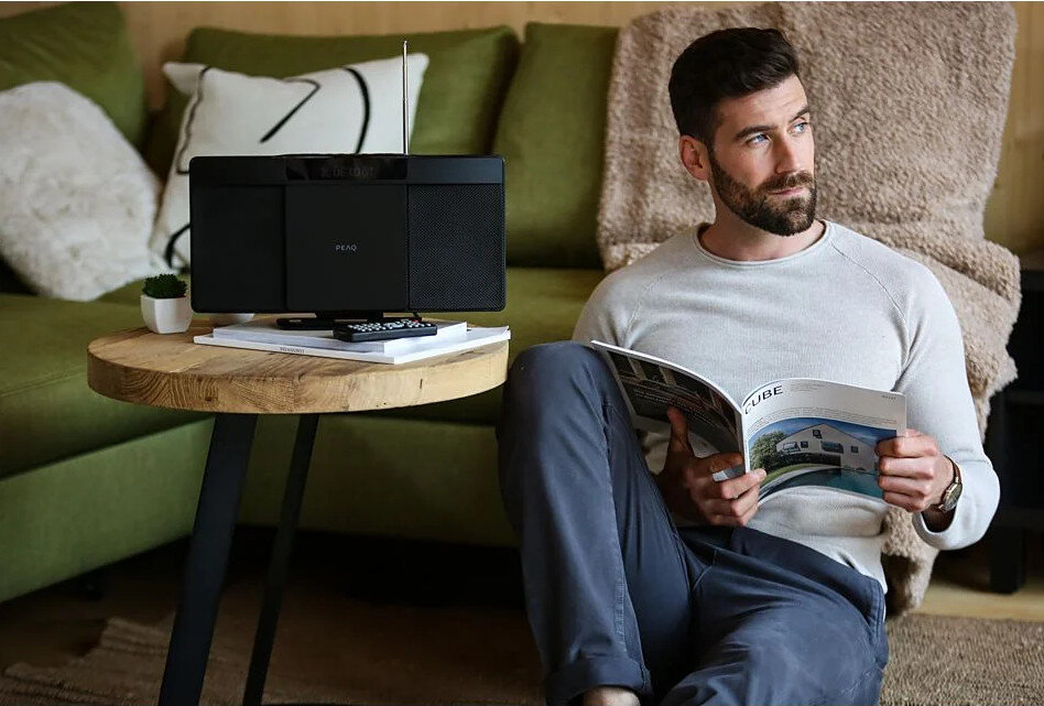 Mężczyzna czyta magazyn w pobliżu czarnego radia z odtwarzaczem CD i pilotem.