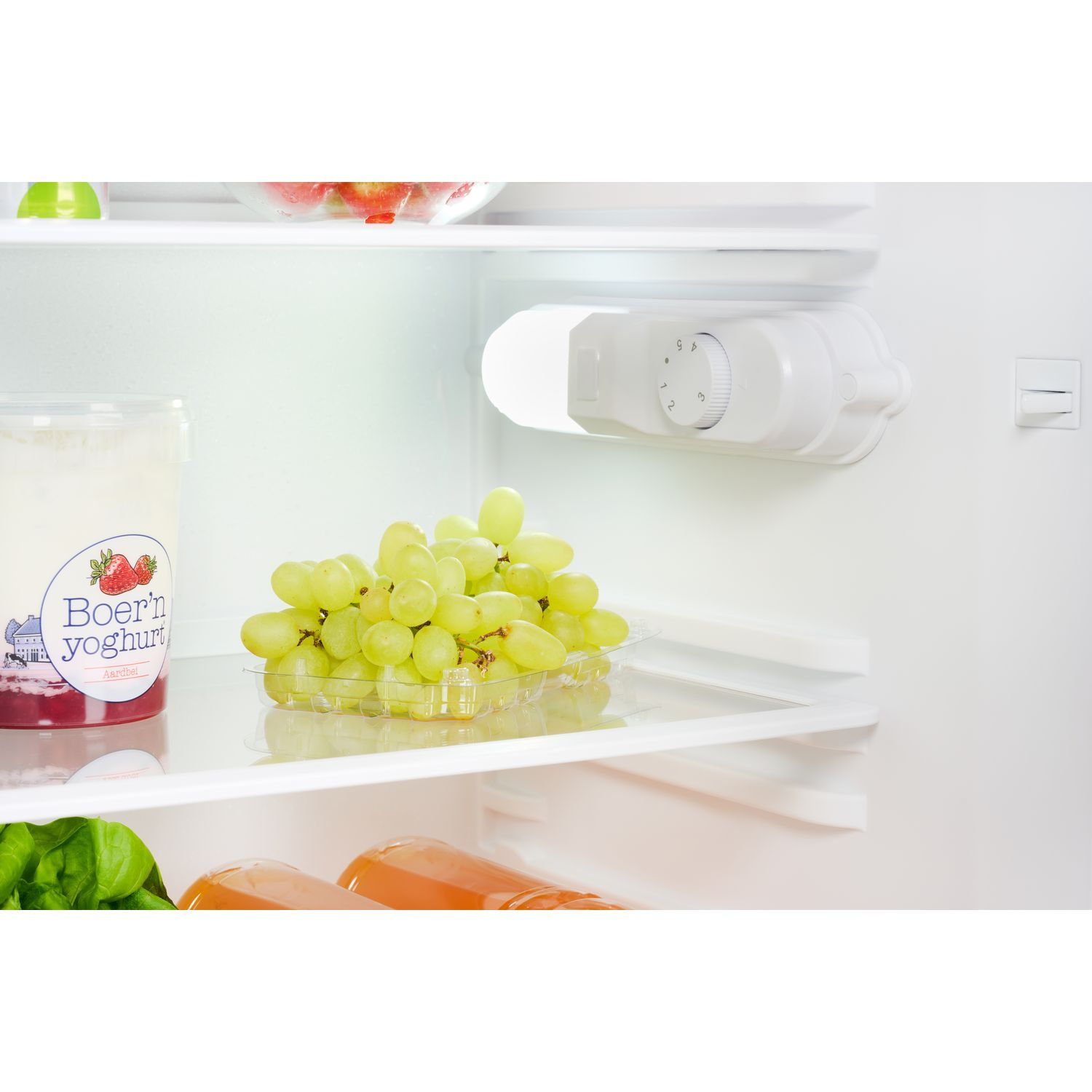Intérieur d'un réfrigérateur avec raisins, yaourt et fruits sur les étagères.