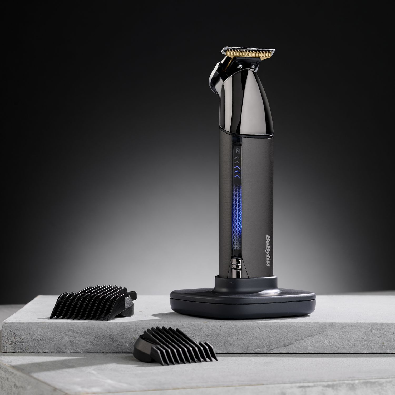 A black and silver Babyliss hair trimmer with two black trimming attachments on a stand.