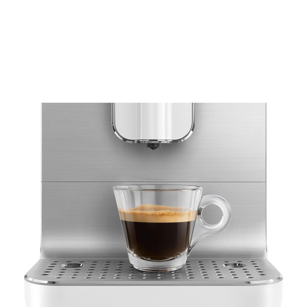 Ein Glas Kaffee steht auf einer silbernen Espressomaschine.
