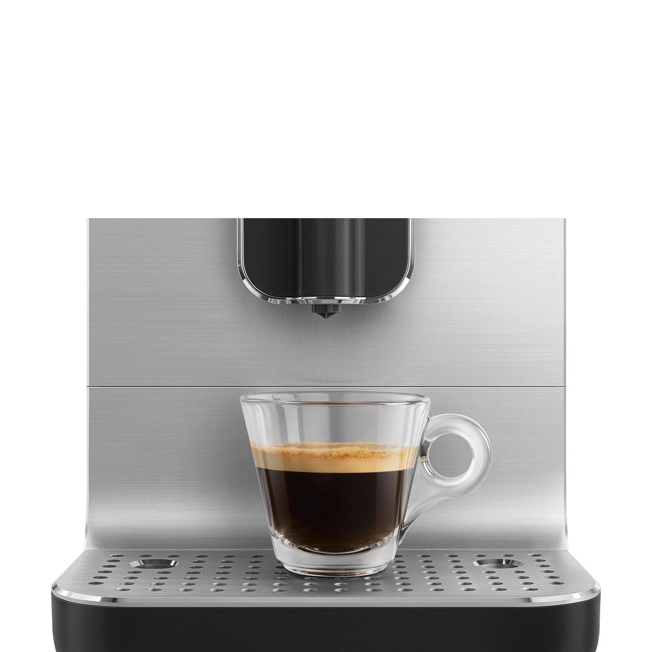 Espresso in einer Glastasse auf einer silbernen Maschine mit schwarzem Oberteil. Weißer Hintergrund.