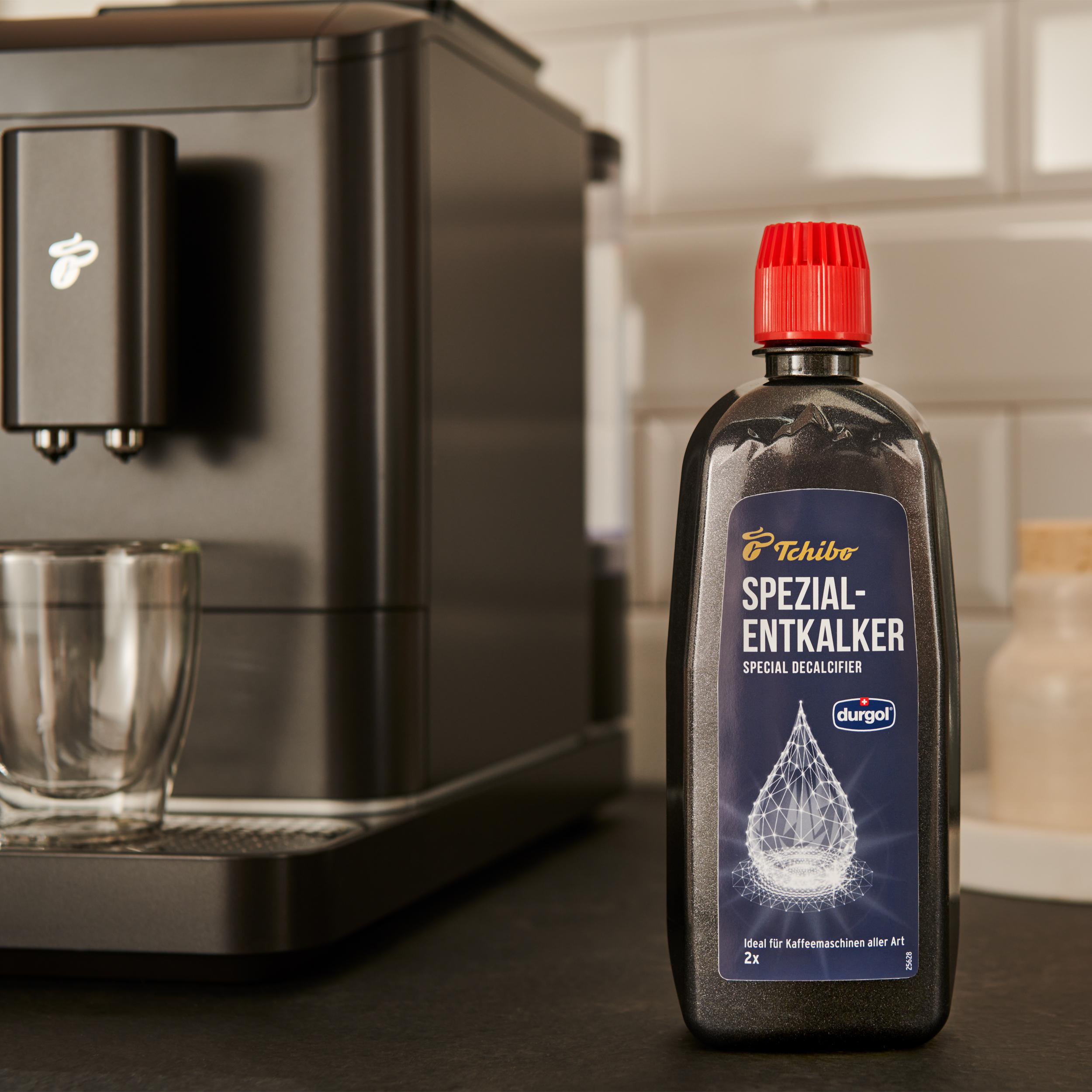 Schwarze Flasche und Kaffeemaschine. Rote Kappe auf der Flasche. Weiße Fliesen im Hintergrund.