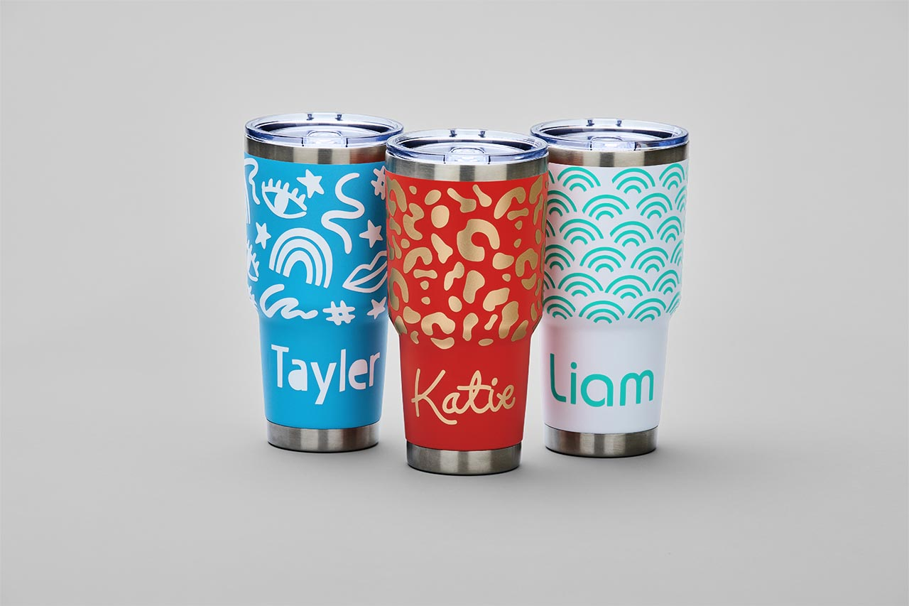 Drei isolierte Becher mit Namen: Tayler (blau), Katie (rot) und Liam (weiß). Jeder hat ein einzigartiges Muster und Deckel.