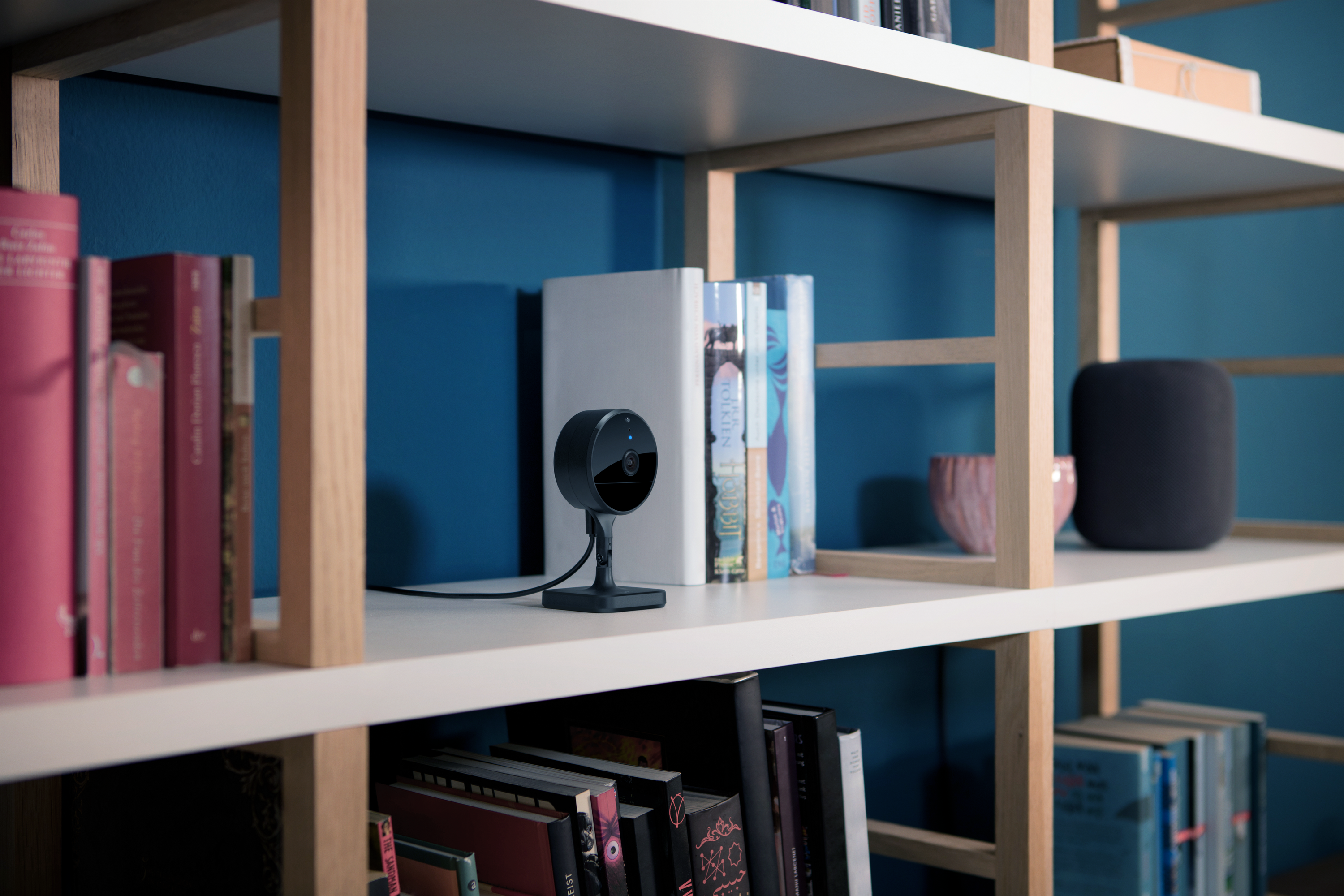 Una telecamera di sicurezza nera si trova su uno scaffale tra libri e una ciotola decorativa.