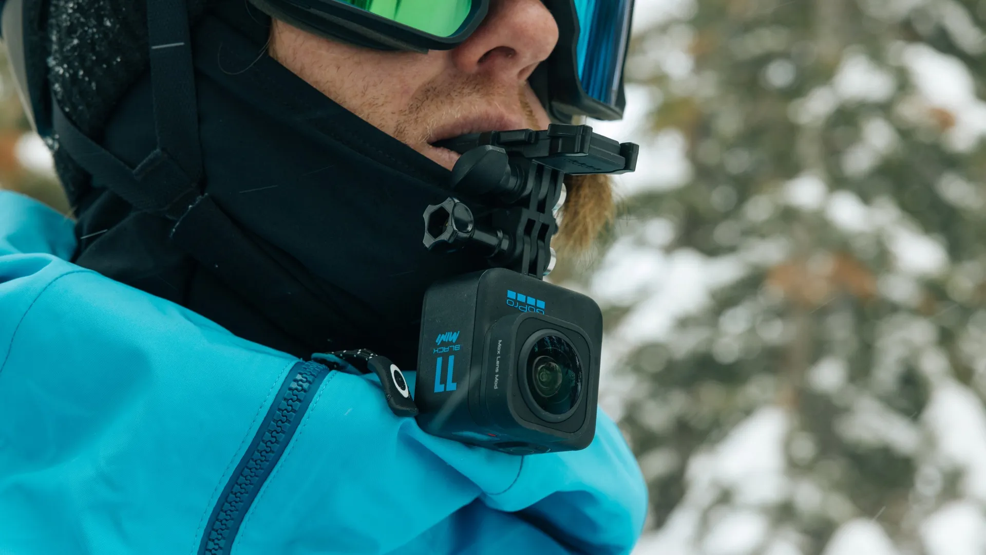 Ein Skifahrer mit Brille und einer am Helm befestigten Kamera, verschneiter Hintergrund.