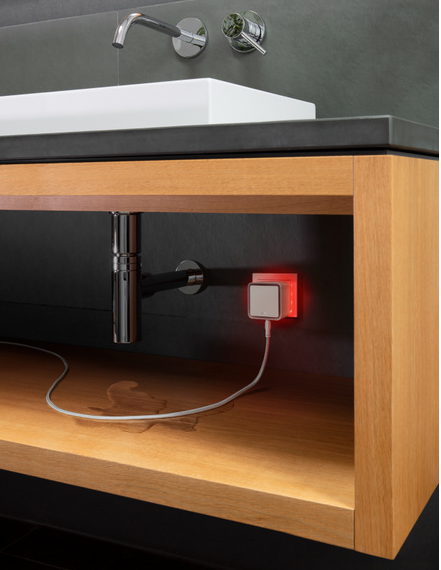Ein weißer Stecker mit rotem Licht, an einem Waschbecken.