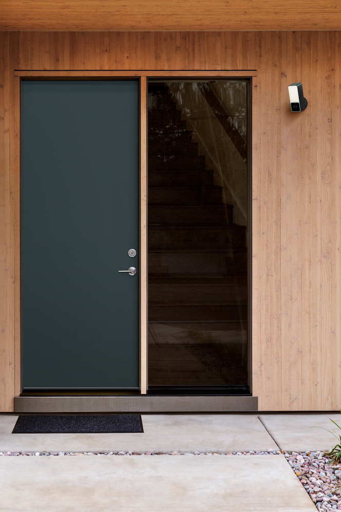 Facciata di casa moderna con porta scura, pannello di vetro e rivestimento in legno. Include uno zerbino.