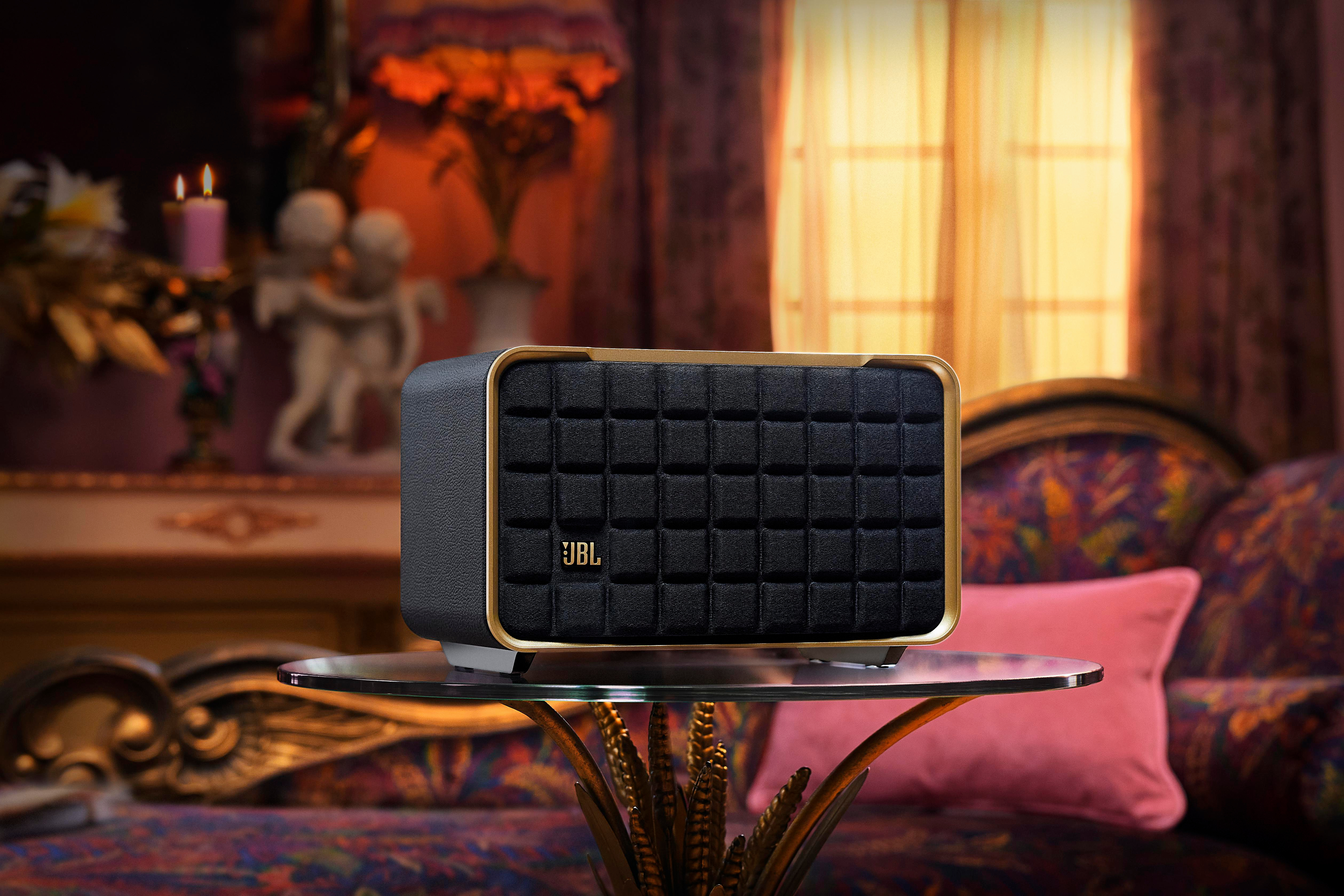 Ein schwarzer JBL-Lautsprecher auf einem Tisch. Er hat eine goldene Zierleiste und steht vor einem Hintergrund.