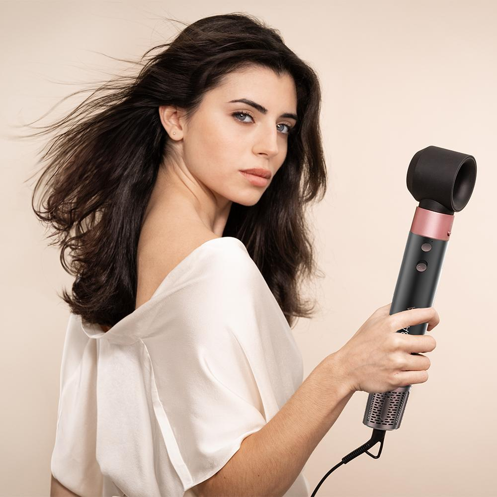 Mujer sosteniendo un secador de pelo negro y oro rosa, mirando a la cámara.