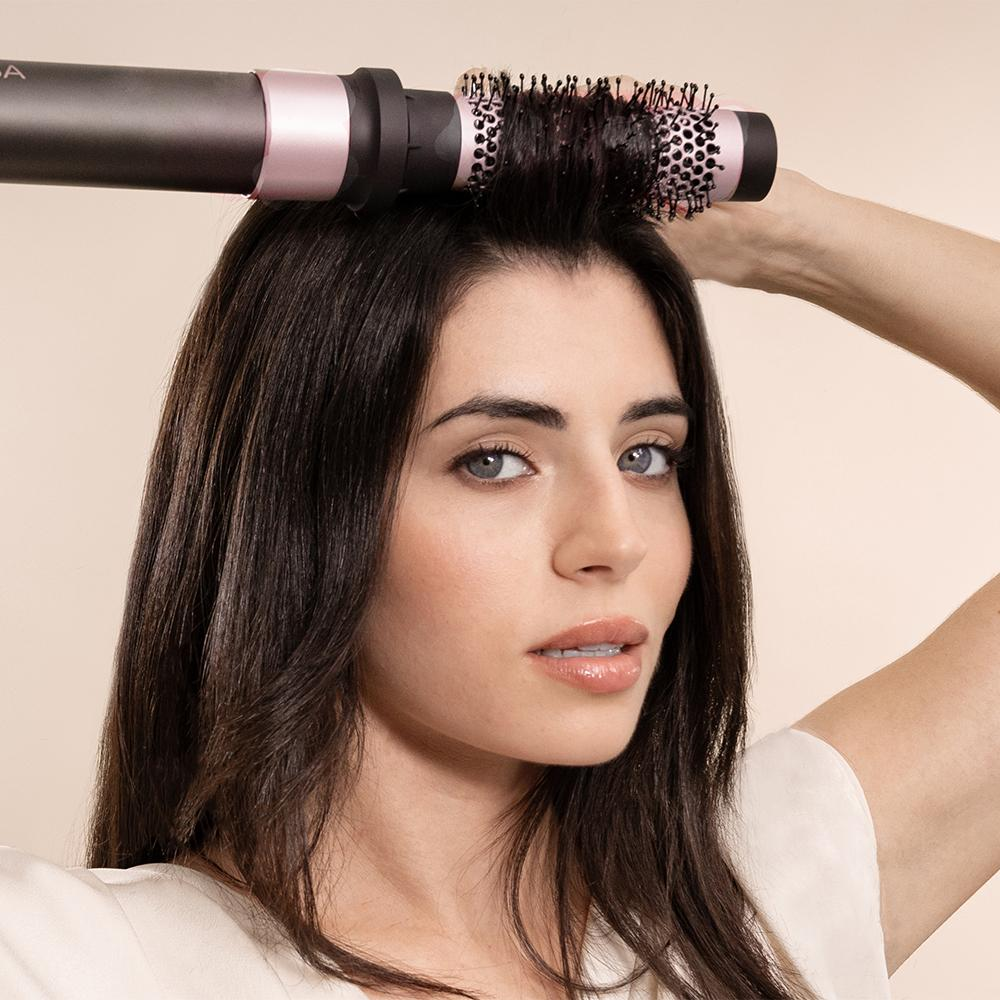 Una mujer peinándose con un cepillo rizador. El cepillo es negro y rosa.