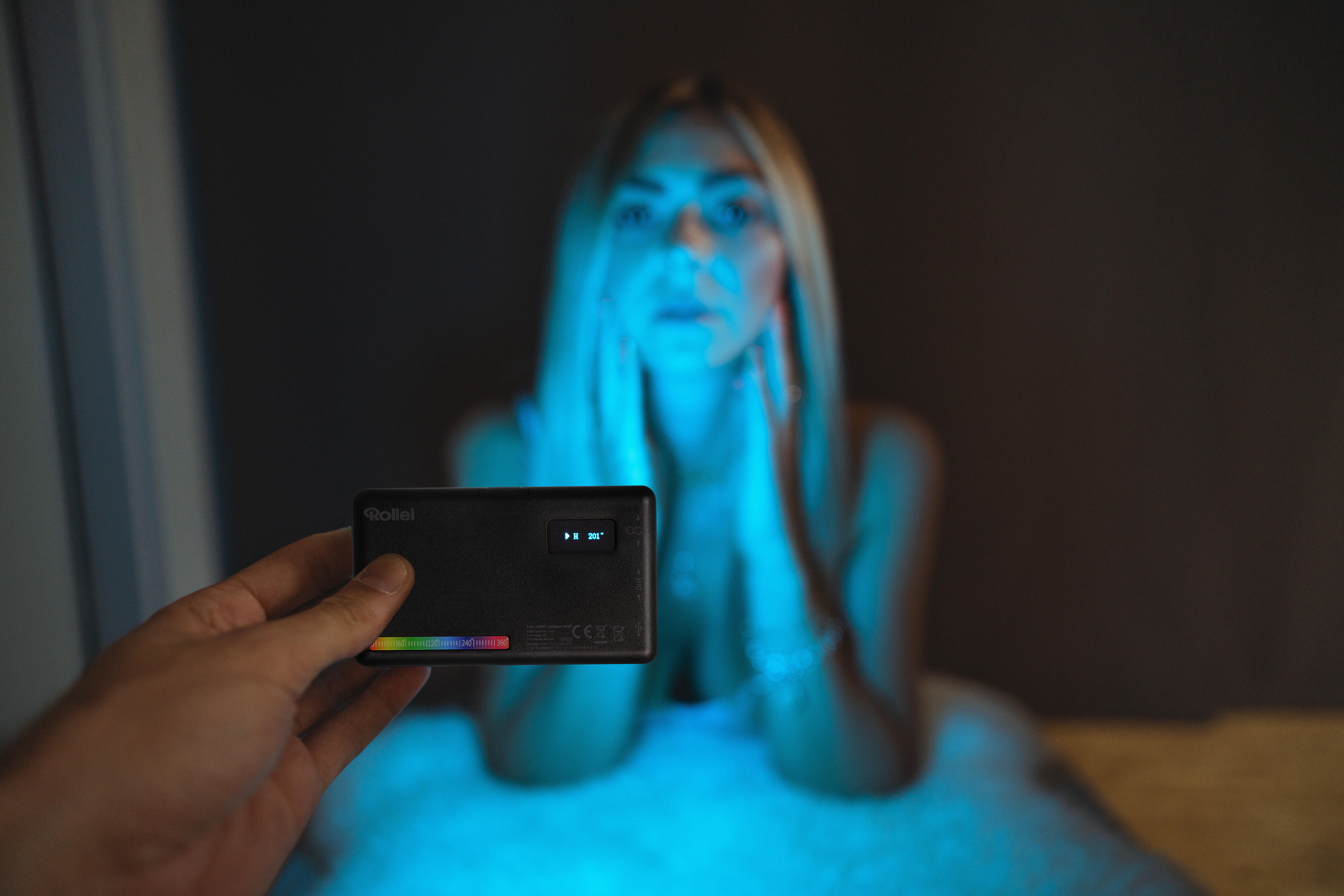 Person hält Rollei-Licht. Blonde Frau im Hintergrund mit blauem Licht beleuchtet.
