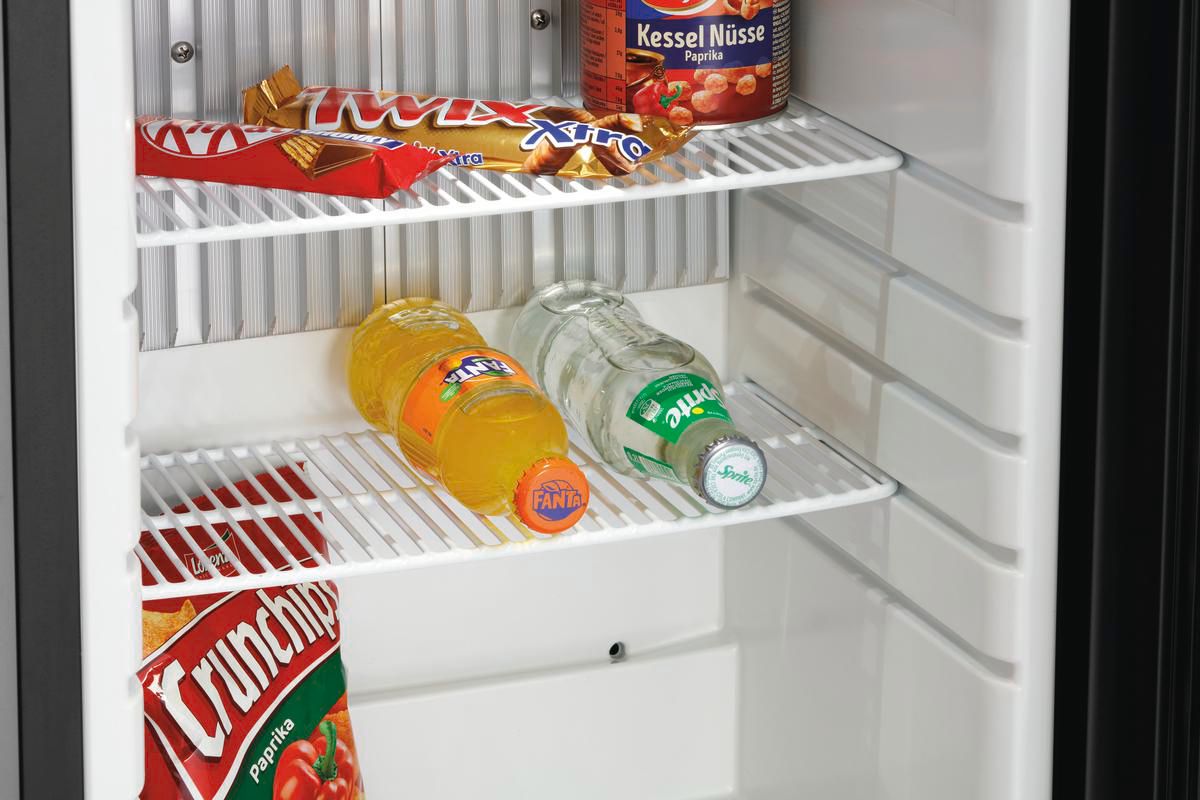 In einem Kühlschrank: Snacks und Getränke. Kit Kat, Twix, Erdnüsse, Fanta, Sprite-Flaschen und eine Tüte Crunchips. Weiße Regale.