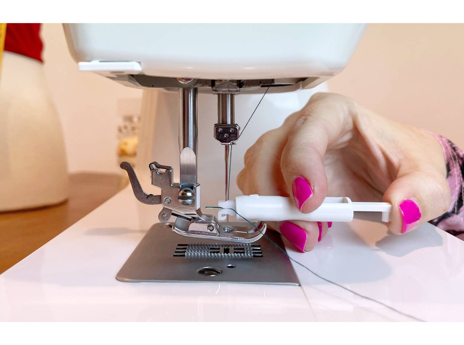 Mano de mujer enhebrando la aguja de una máquina de coser con una herramienta de plástico blanco.