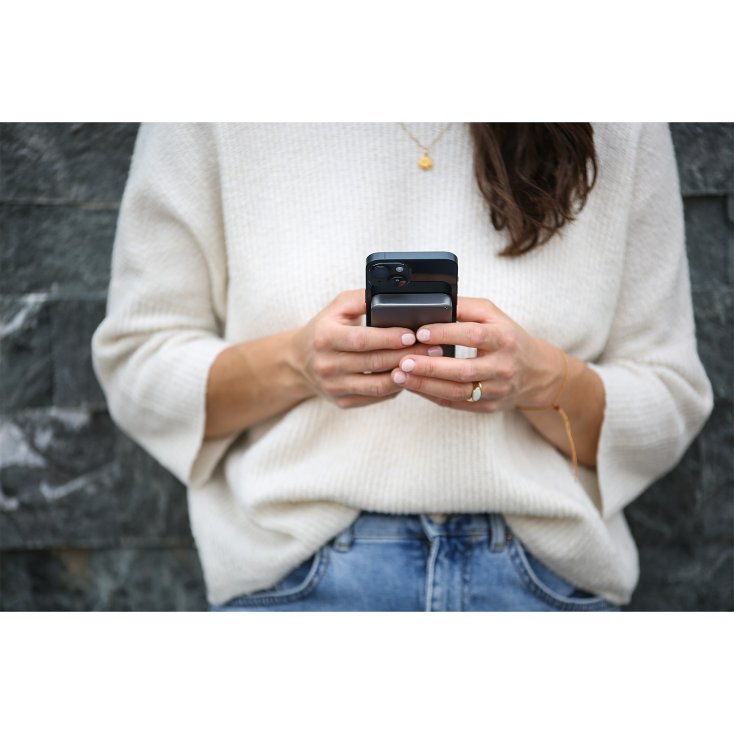 Una persona tiene in mano un telefono e un power bank nero davanti a un muro grigio strutturato.