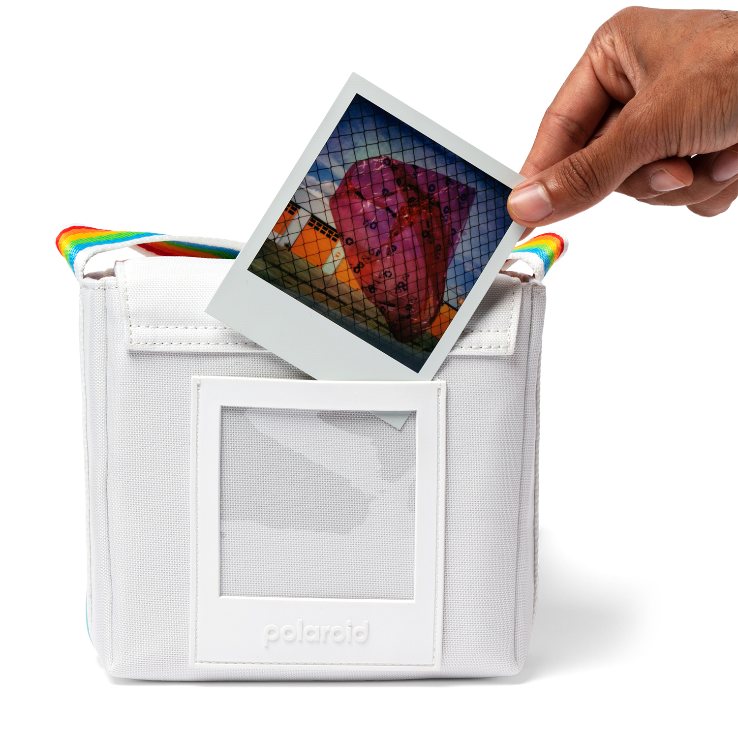 Una mano che tiene una foto polaroid sopra una borsa bianca. L'immagine è di una scena colorata.
