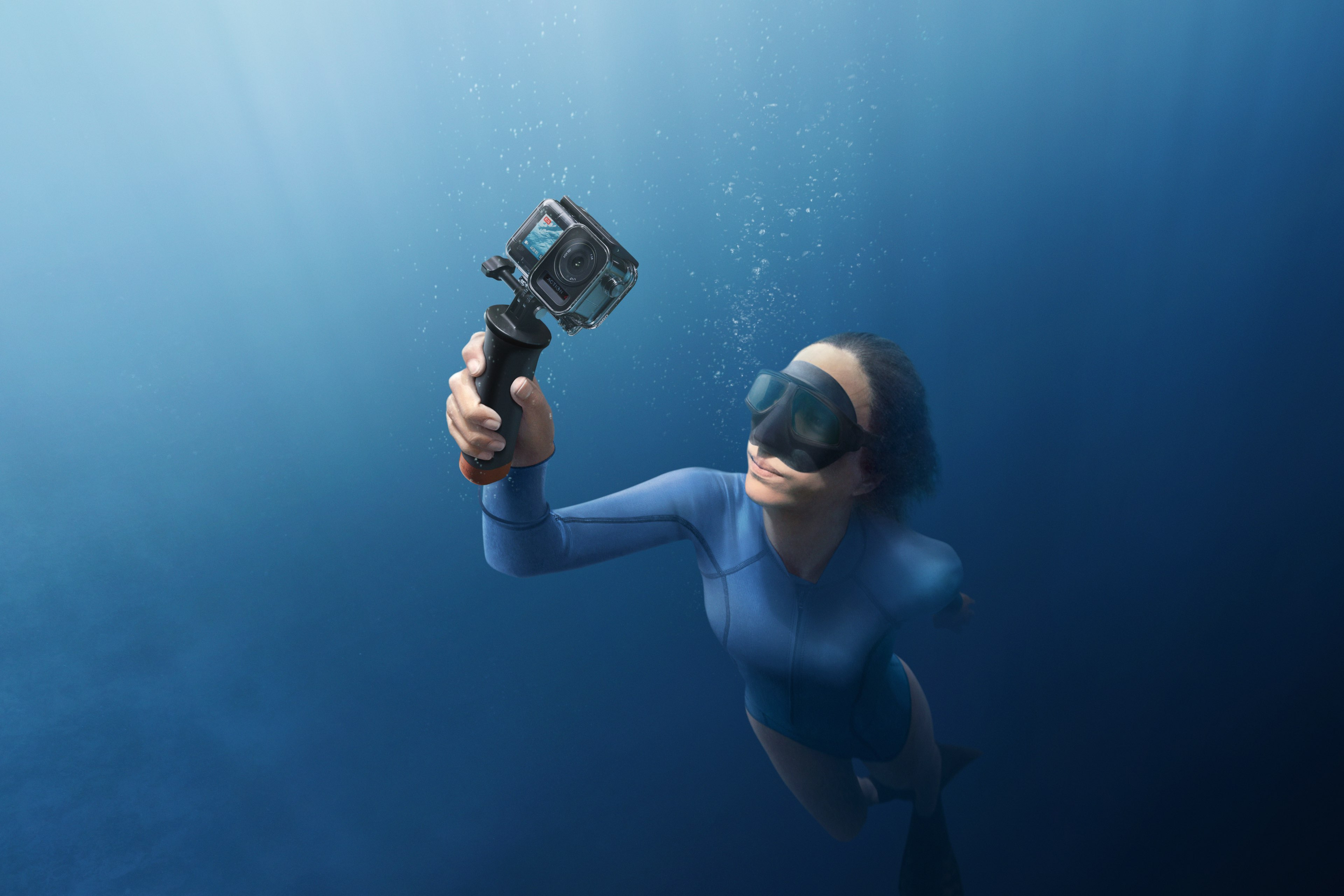 Frau taucht in blauem Wasser und hält eine Kamera in einem wasserdichten Gehäuse.