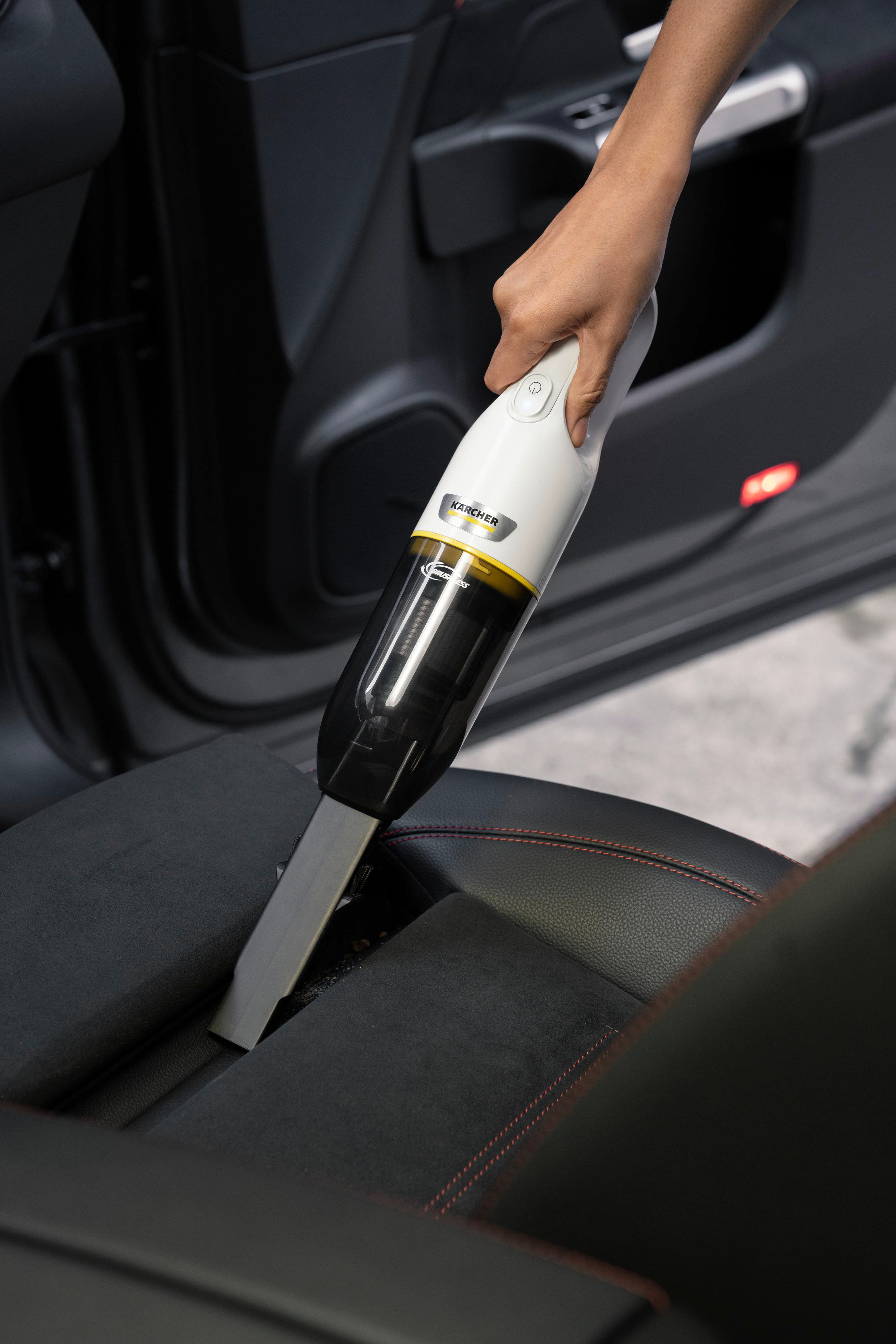 Hand benutzt weißen Staubsauger im Auto auf schwarzem Autositz. Rote Nähte sichtbar.