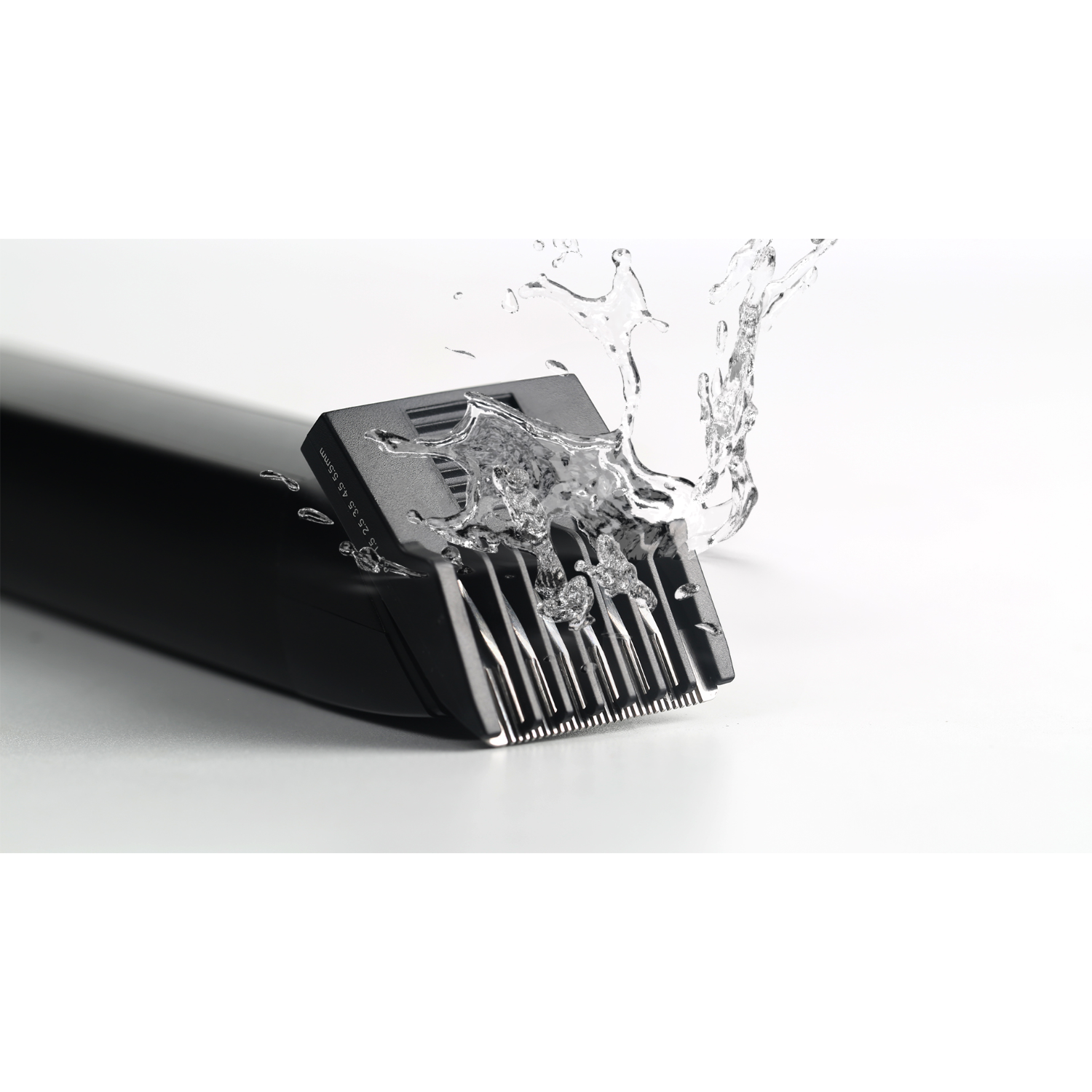 A black electric razor head with water splashing on it. White background.