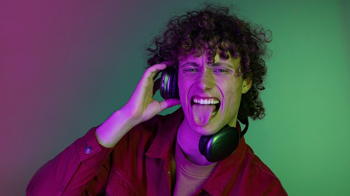 Uomo con le cuffie, che tira fuori la lingua, con illuminazione verde e viola.