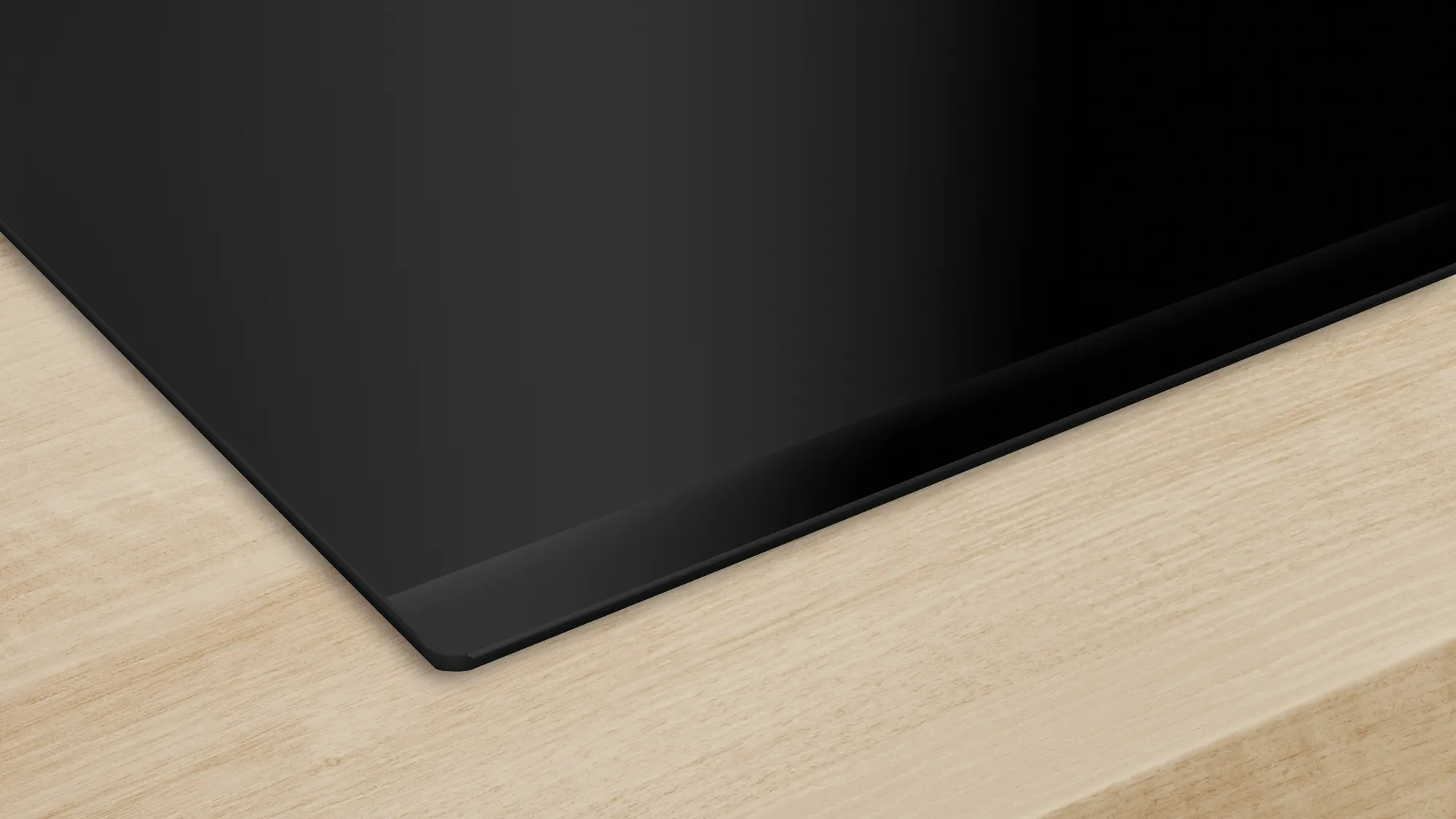 Egy fekete főzőlap világos fa pulton, sötét szegéllyel.