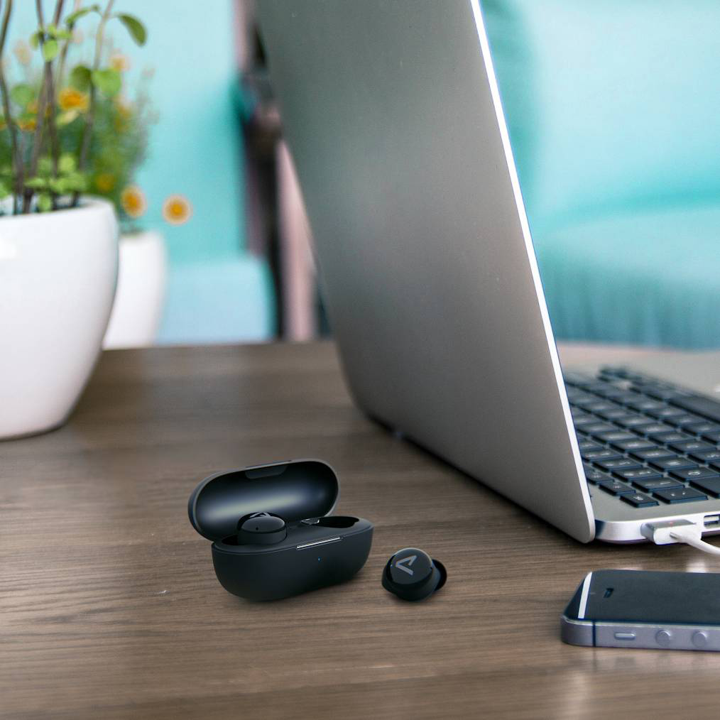 Fekete fülhallgatók a tokban egy laptop és telefon mellett egy fa asztalon.