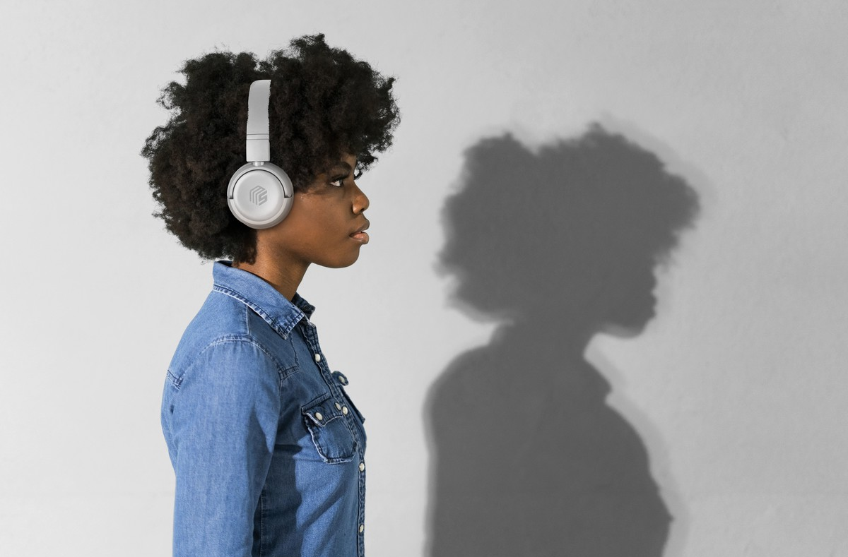 Femme en chemise en jean portant un casque blanc, vue de profil, fond gris, ombre sur le mur.