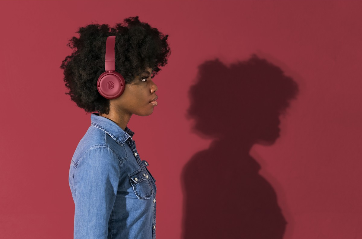 Femme de profil portant un casque rouge et une chemise en jean, sur fond rouge.