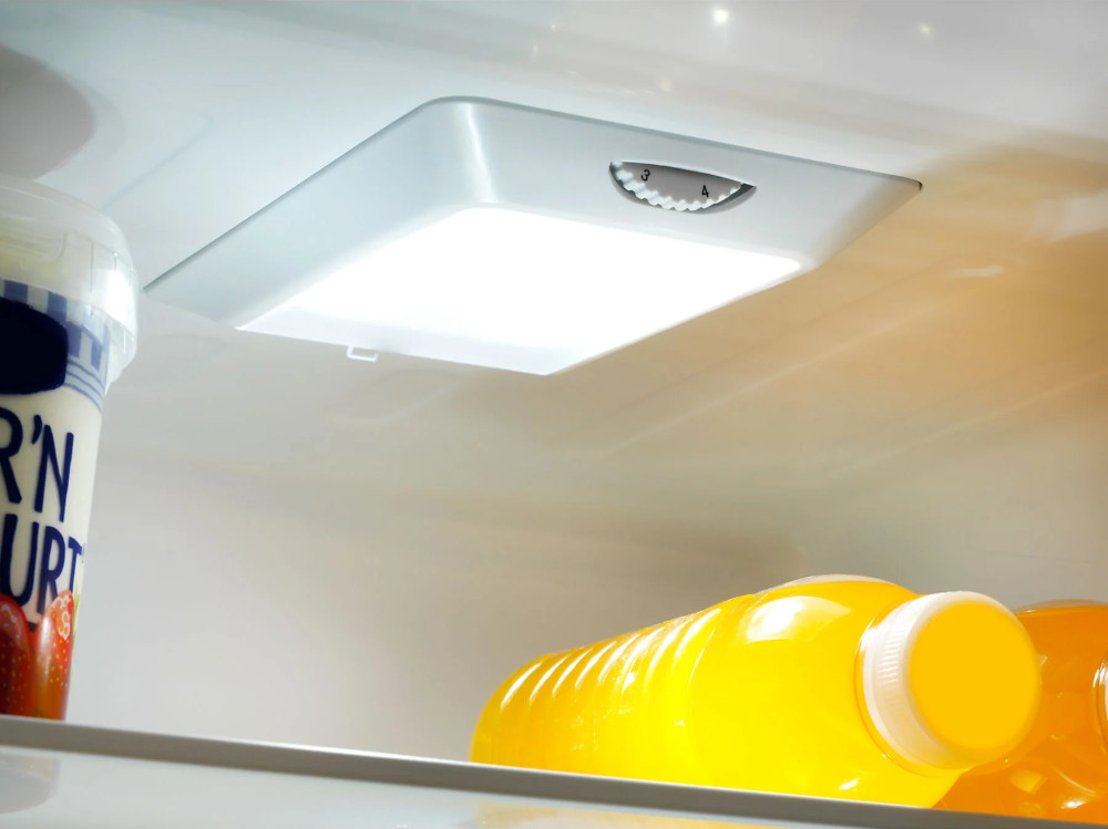 Interior refrigerator light.  Light is square-shaped. Orange juice and yogurt are nearby.