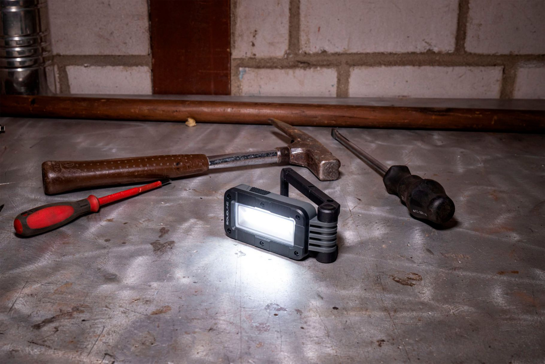 Werkstattszene mit Lampe, Hammer, Schraubendrehern auf Metalloberfläche.